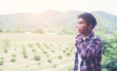 Hipster adam duman sigara, bir dağın duruyor. Sabah temiz havada arasında.