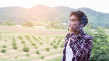 Hipster adam duman sigara, bir dağın duruyor. Sabah temiz havada arasında.