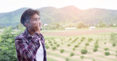 Hipster adam duman sigara, bir dağın duruyor. Sabah temiz havada arasında.
