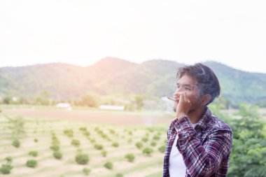 Hipster adam duman sigara, bir dağın duruyor. Sabah temiz havada arasında.