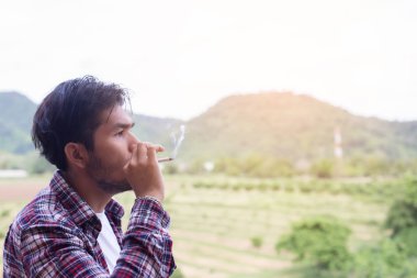 Hipster adam duman sigara, bir dağın duruyor. Sabah temiz havada arasında.