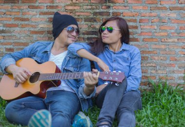 Kız arkadaşı için açık tuğla duvara gitar hipster adam birlikte zevk.