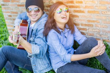 Kız arkadaşı için açık tuğla duvara gitar hipster adam birlikte zevk.