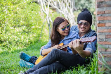 Kız arkadaşı için açık tuğla duvara gitar hipster adam birlikte zevk.