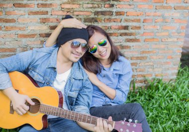 Kız arkadaşı için açık tuğla duvara gitar hipster adam birlikte zevk.