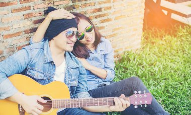 Kız arkadaşı için açık tuğla duvara gitar hipster adam birlikte zevk.