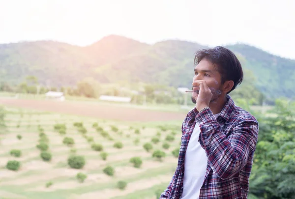 Hipster adam duman sigara, bir dağın duruyor. Sabah temiz havada arasında.