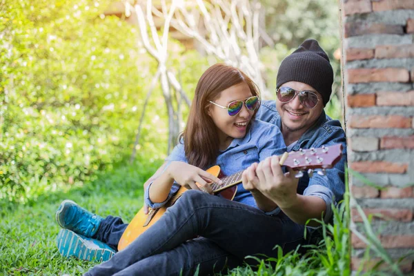 Kız arkadaşı için açık tuğla duvara gitar hipster adam birlikte zevk.