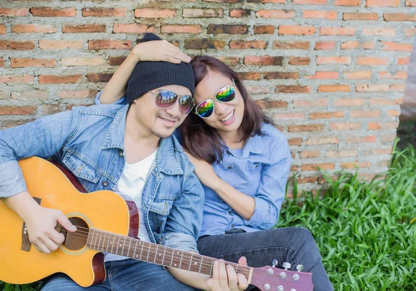 Kız arkadaşı için açık tuğla duvara gitar hipster adam birlikte zevk.
