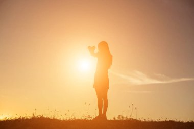 Gün batımı siluetiyle kalp şeklinde eller.