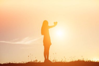 Gün batımı siluetiyle kalp şeklinde eller.