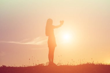 Gün batımı siluetiyle kalp şeklinde eller.