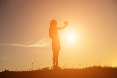 Gün batımı siluetiyle kalp şeklinde eller.