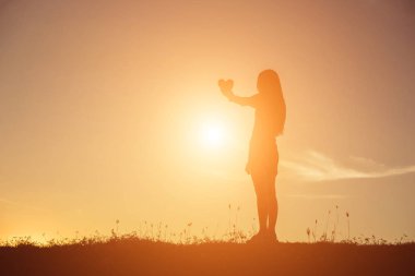 Gün batımı siluetiyle kalp şeklinde eller.