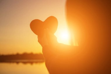 Gün batımı siluetiyle kalp şeklinde eller.
