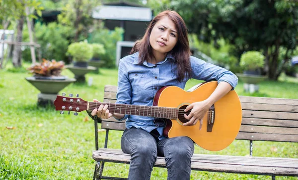 Güzel genç kadın mutlu zaman kavramı banktaoturuyor gitar çalmak.