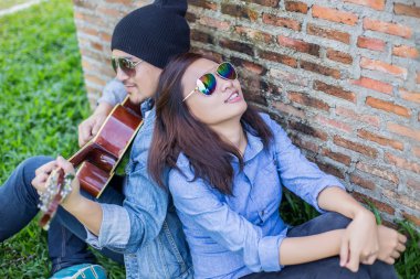 Kız arkadaşı için açık tuğla duvara gitar hipster adam birlikte zevk.