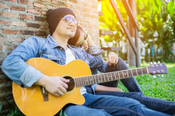 Kız arkadaşı için açık tuğla duvara gitar hipster adam birlikte zevk.