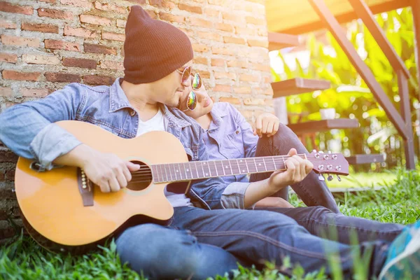 Kız arkadaşı için açık tuğla duvara gitar hipster adam birlikte zevk.