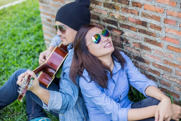 Kız arkadaşı için açık tuğla duvara gitar hipster adam birlikte zevk.