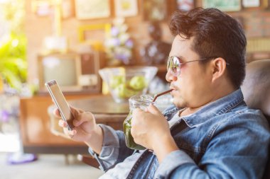 Café'de rahatlatıcı gülümseyen smartphone ile genç adam.