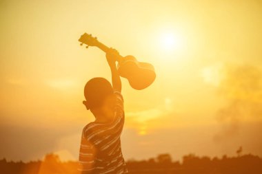 Gün batımı gitarı tutan çocuk ayakta