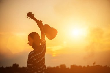 Gün batımı gitarı tutan çocuk ayakta