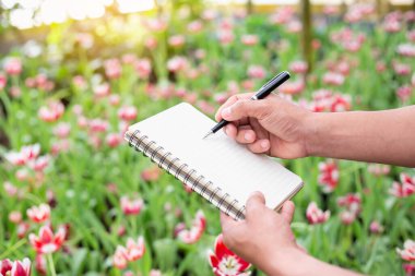 Beyaz bir çiçek bahçesinde notlar alan bir kadın