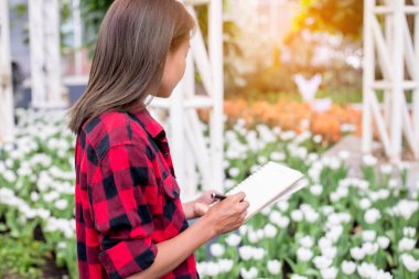 Beyaz bir çiçek bahçesinde notlar alan bir kadın