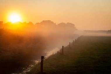 Hollanda 'da güzel sisli bir sabah. Turuncu bir güneş doğuyor ve çiftçi topraklarında küçük bir hendek var. Fotoğraf Overijssel' de çekildi.