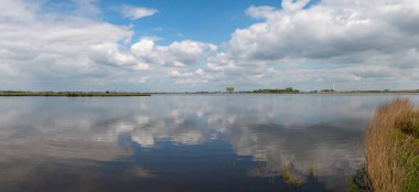 Hollanda 'da, Friesland bölgesi Gaasterland' da güzel bir göl manzarası. Mavi gökyüzünün yansıması ve sudaki beyaz bulutlarla