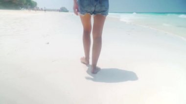 Okyanus boyunca kum plajındaki yalınayak kız yürüyor