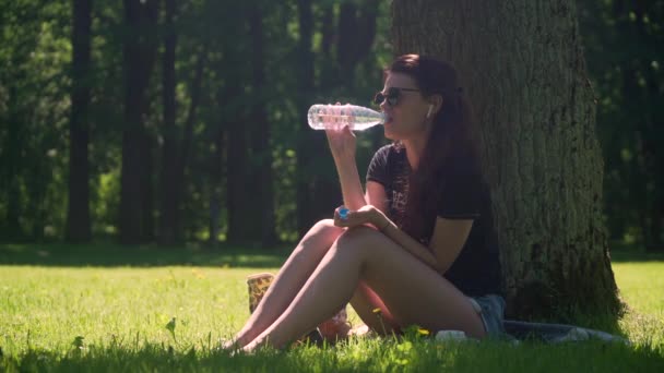 Young woman drinking water from bottle in park — Stock Video