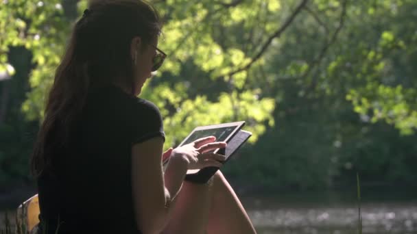 Mujer joven en el parque usando tableta digital — Vídeo de stock