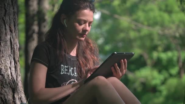 Mujer joven en el parque utiliza tableta para el estudio y el trabajo — Vídeos de Stock