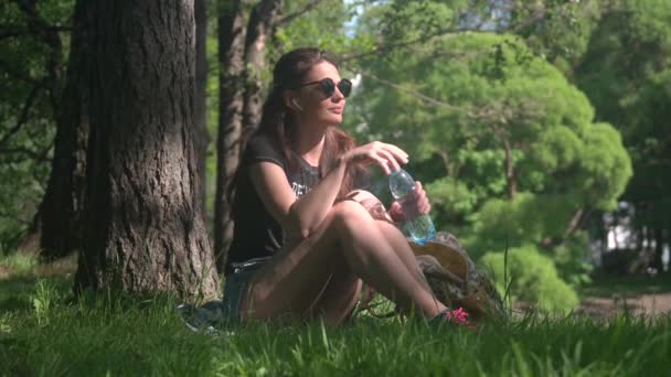 Junge Frau trinkt Wasser aus Flasche im Park — Stockvideo