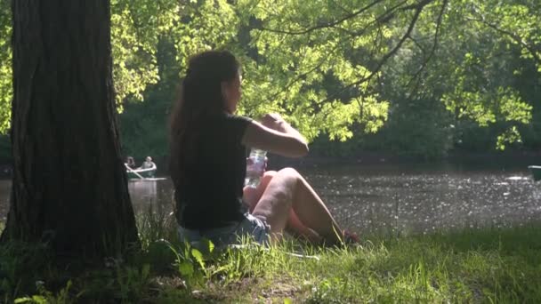 Jeune femme eau potable de la bouteille dans le parc — Video