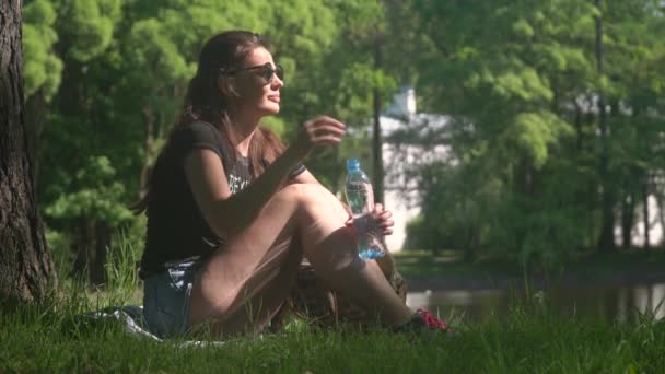 Junge Frau trinkt Wasser aus Flasche im Park — Stockvideo