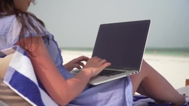 Young woman uses laptop on white beach near ocean — Stok video