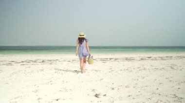 Young woman walks barefoot on beach towards ocean