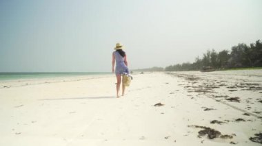 Young woman walks barefoot on beach along ocean
