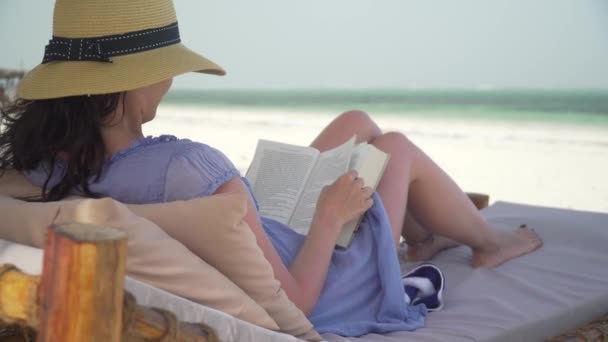 Young woman reading book on white beach by ocean. — Stock Video