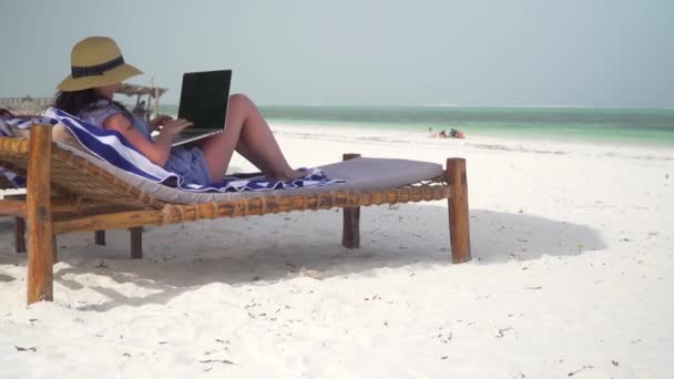 Young woman uses laptop on white beach near ocean — Stockvideo