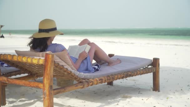 年轻女子在海边的白沙滩看书. — 图库视频影像