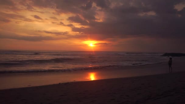 Felnőtt lány sziluettje sétál a tengerparton naplementekor — Stock videók