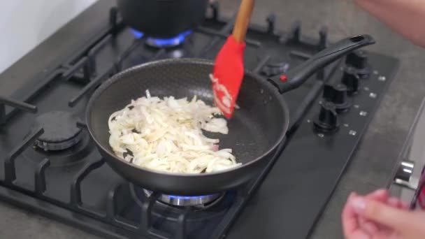 Молодая женщина перемешивает жареный лук в горячей сковороде — стоковое видео