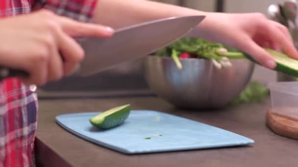 Молодая домохозяйка режет огурец на пластиковой доске — стоковое видео