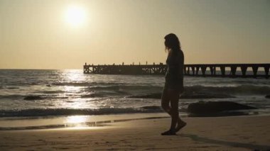 Kadın siluet gün batımında deniz kıyısında yürür