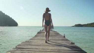 Kadın tropik plajda ahşap iskele üzerinde yürüyor