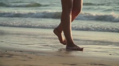 Gün batımında sahilde yürüyen kadın bacakları yakın çekim